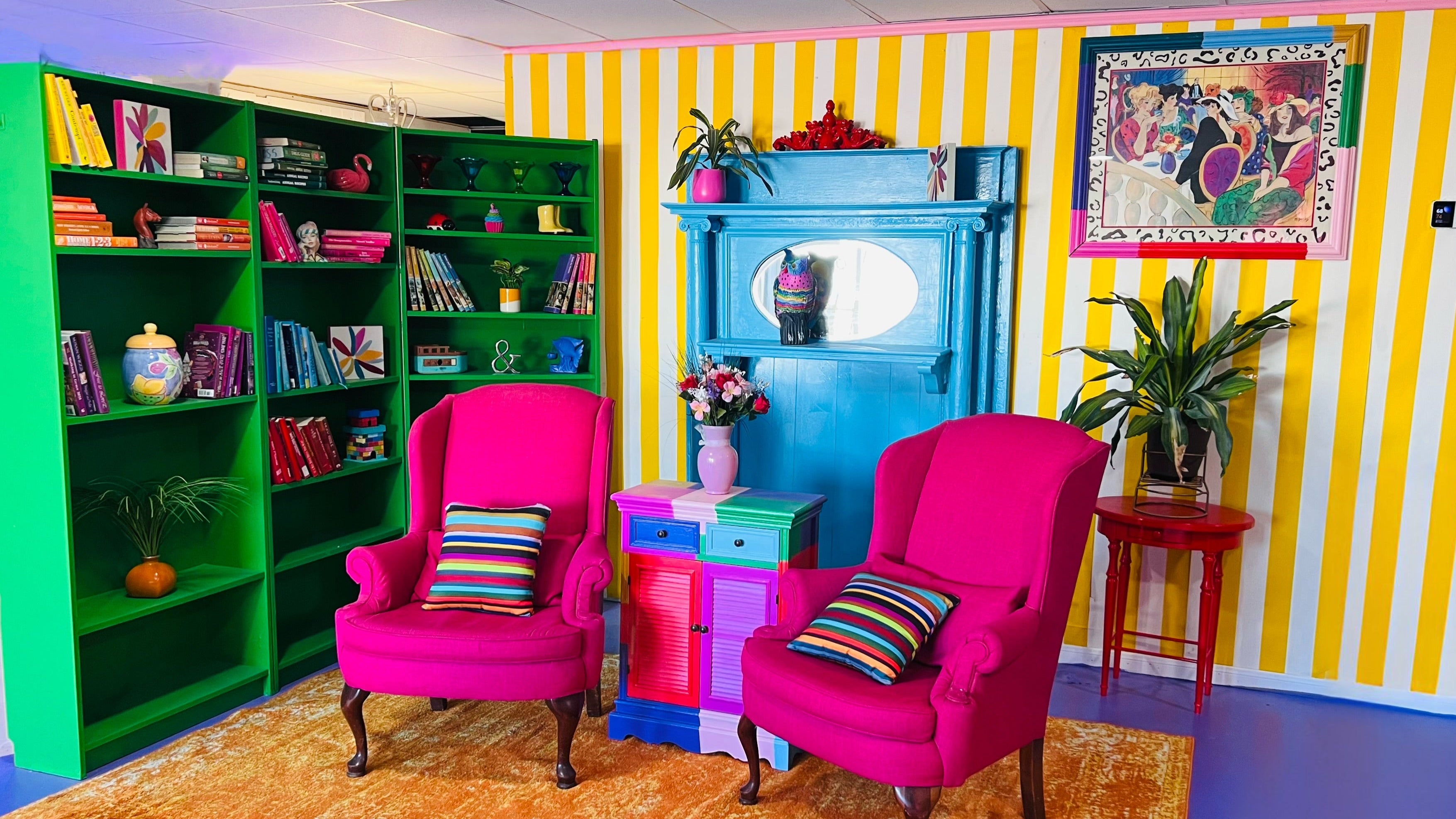 Colorful room with striped walls, pink chairs, and a green bookshelf.